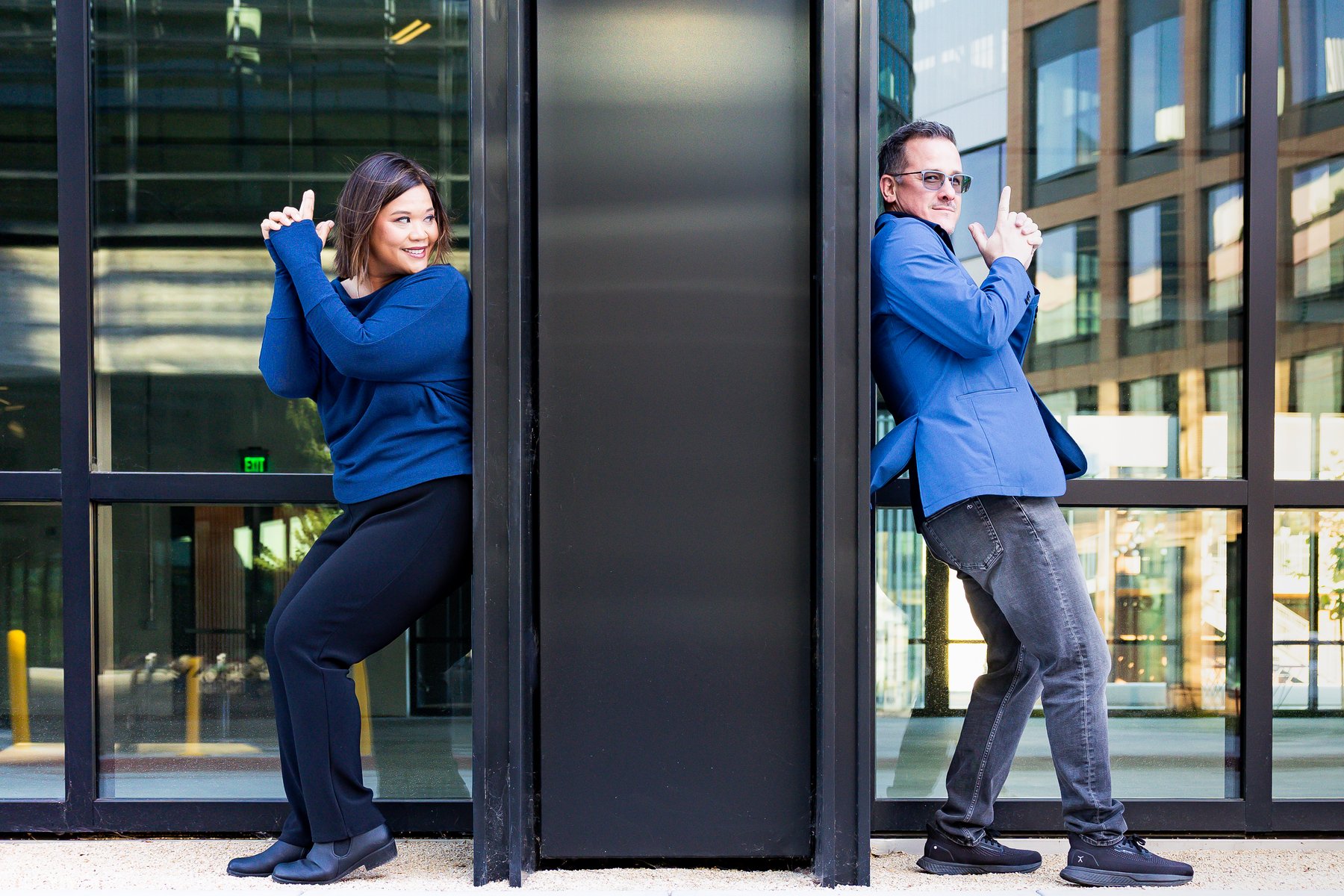Patrick Donato and Arlene Pineda back to back in a playful finger-guns pose, split by a black steel column.