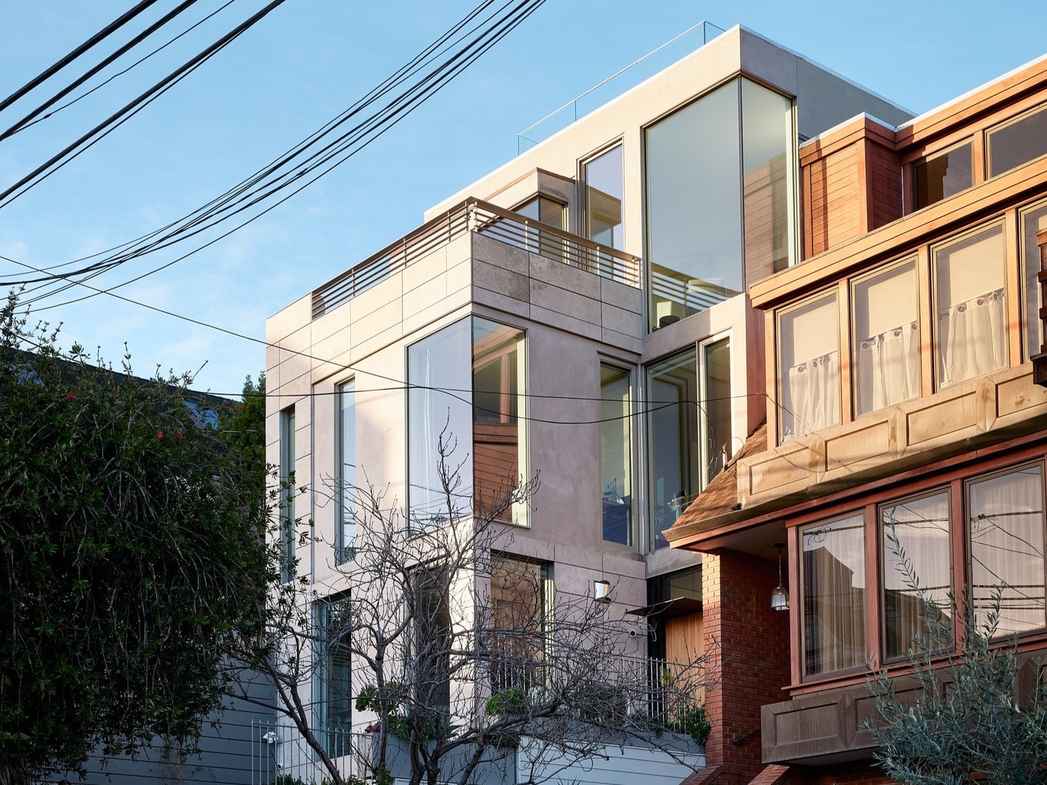 Kansas Street: modern stucco-and-wood volume beside a red-brick craftsman, daytime exterior.