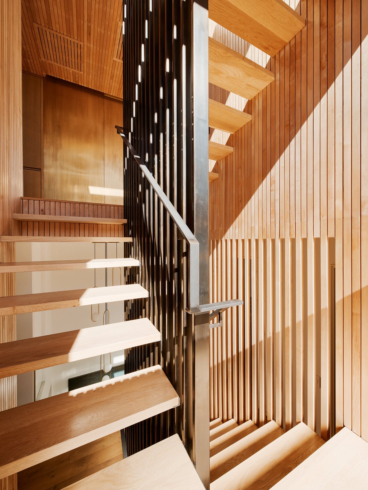 Custom stair with wood treads and a blackened-steel stringer, rising through the cedar-slat enclosure.