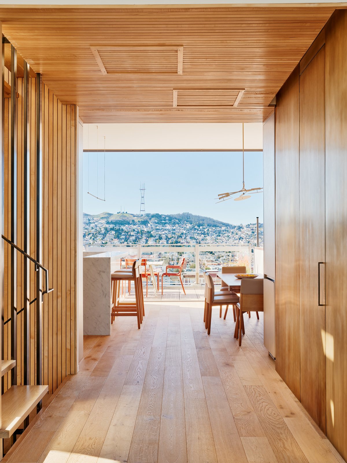 View from the living room past the kitchen's marble counter and dining table to the terrace deck, with Twin Peaks and Sutro Tower beyond.