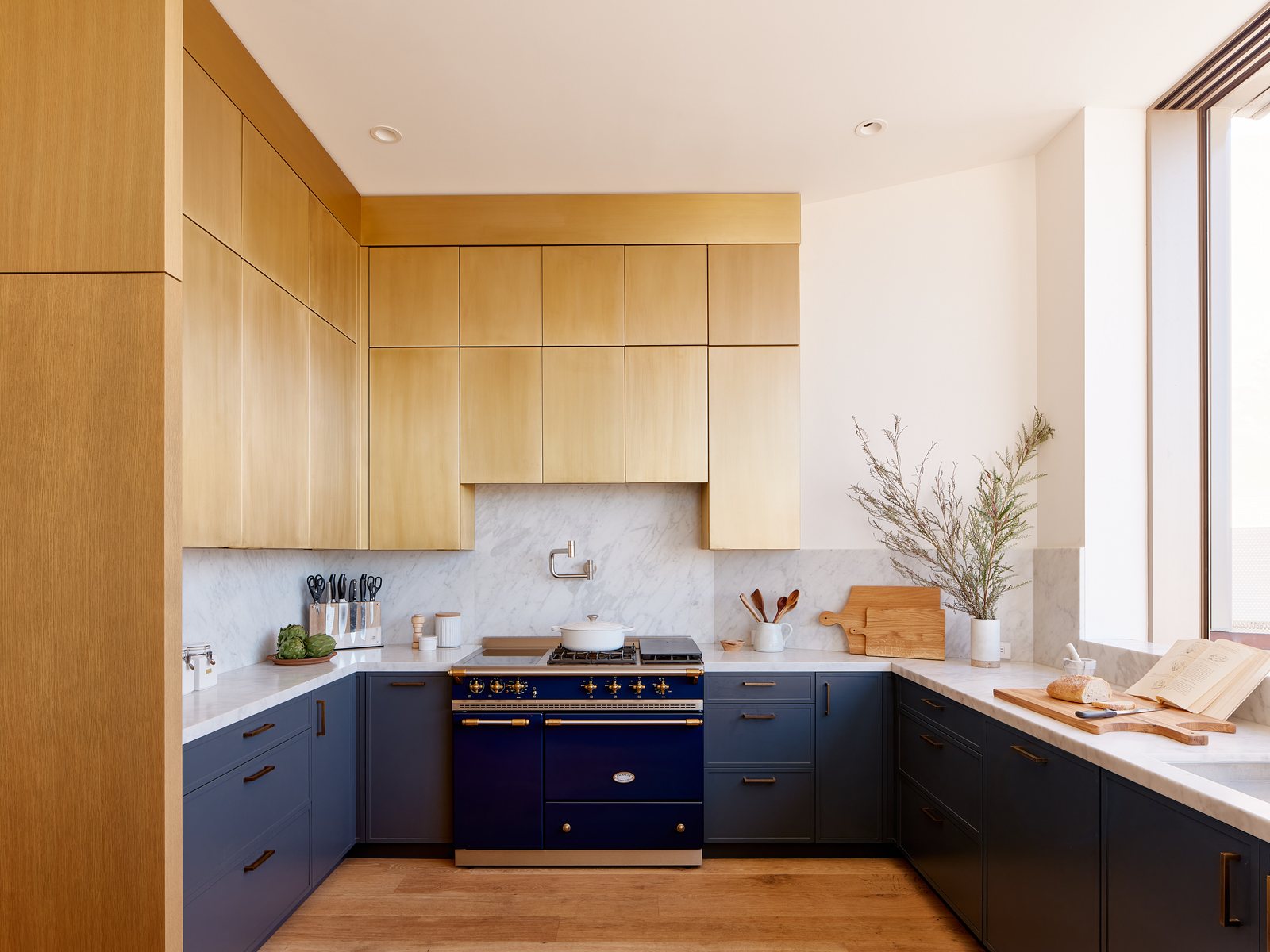 Kitchen with marble counters, a navy range, oak cabinetry, and brass fittings.