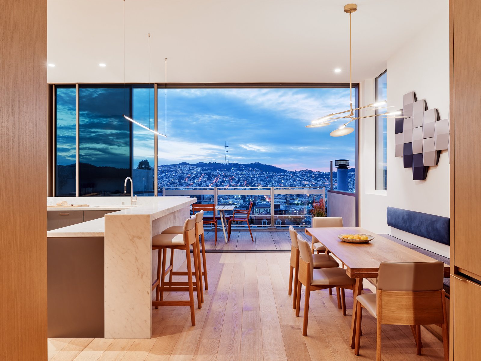 Kansas Street: kitchen, dining room, and bay view at twilight, with a marble island, brass pendants, and the city of San Francisco beyond.
