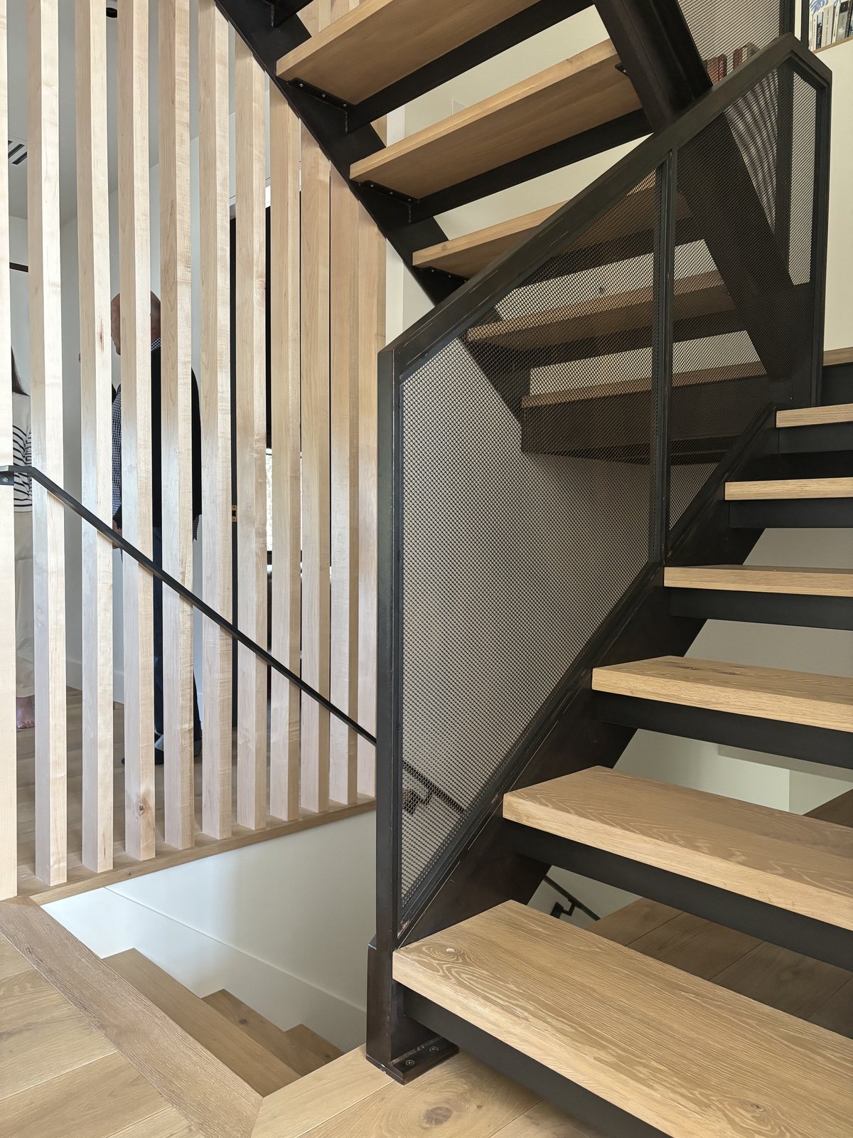 Custom staircase viewed from above: wood treads, blackened-steel frame, perforated metal balustrade.
