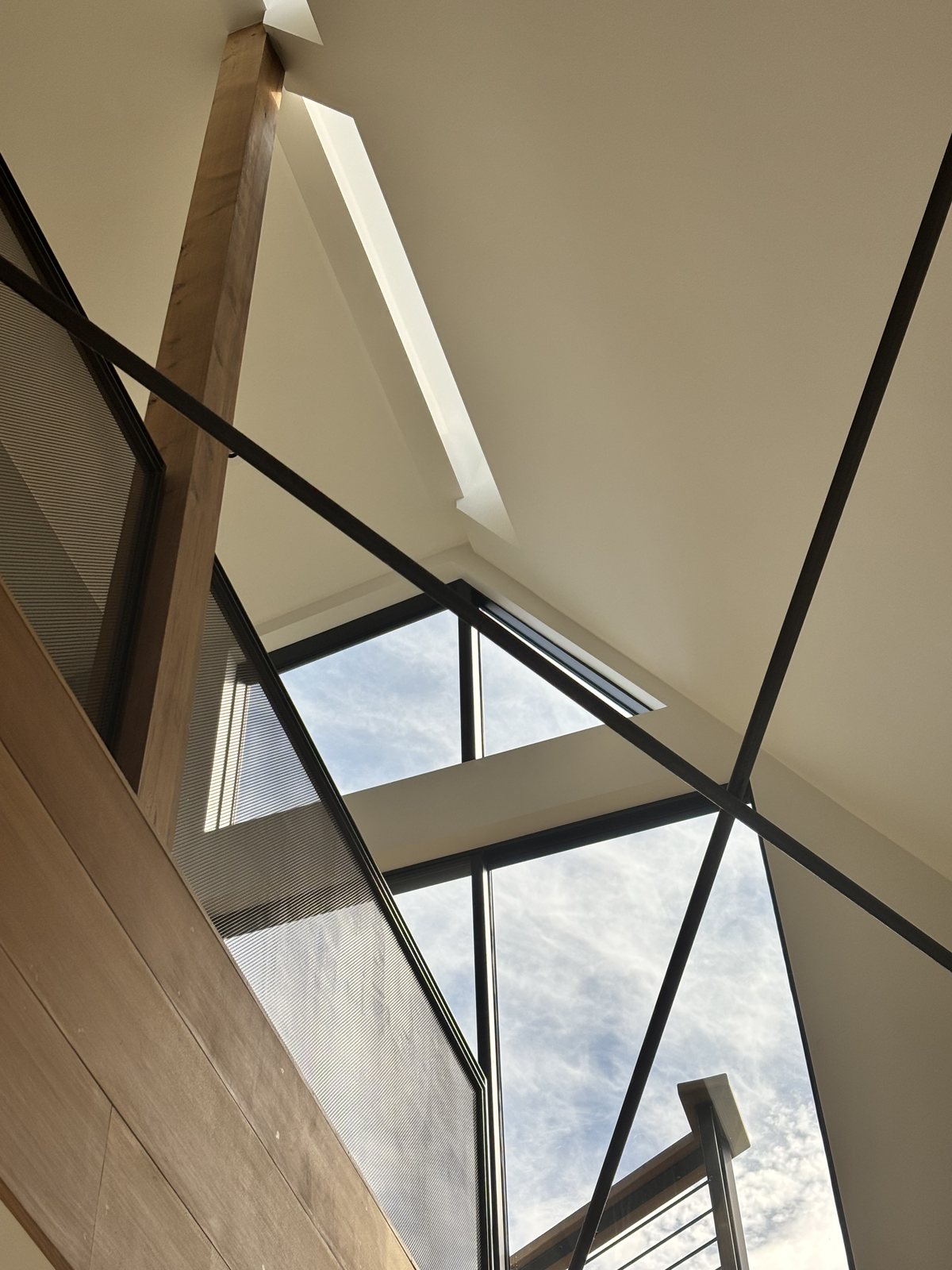 Angular clerestory skylight cutting through the double-height interior, exposed black-steel scissor structure framing sky.